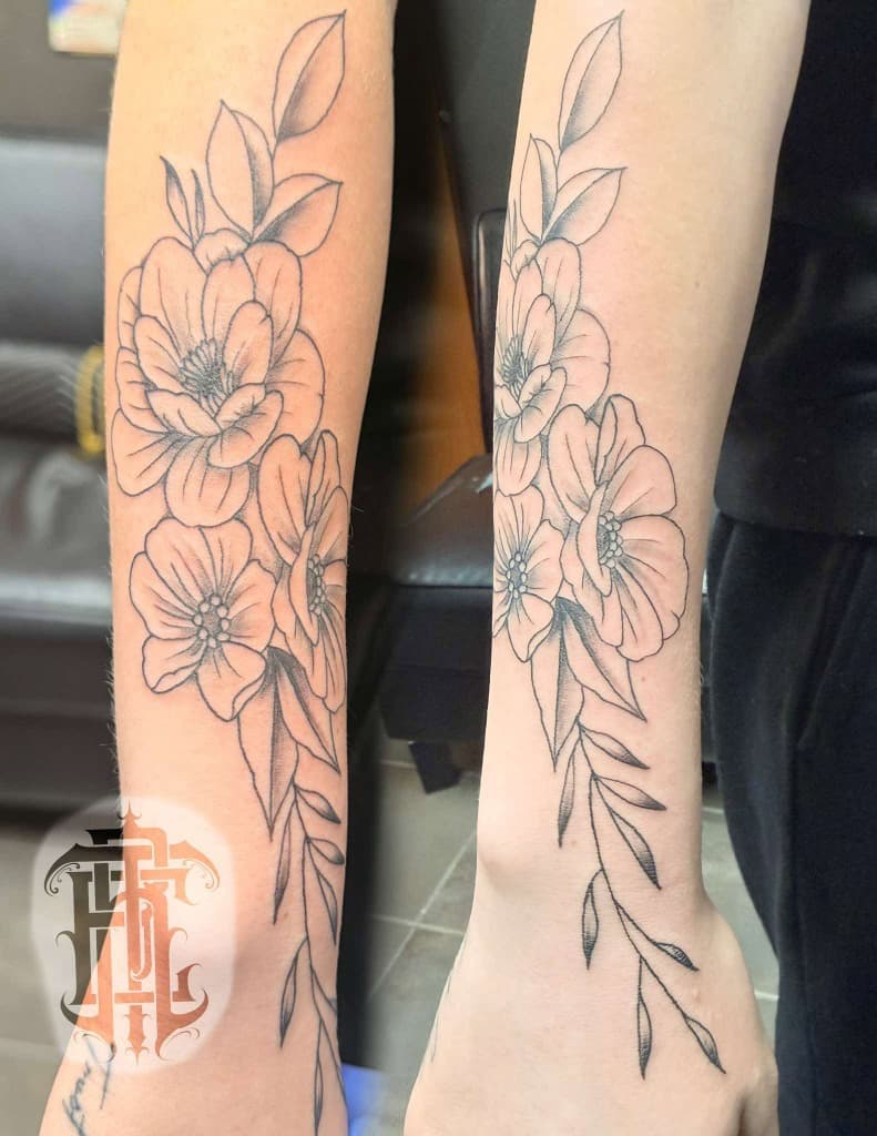 Fine-line botanical tattoo with flowers and leaves along an arm